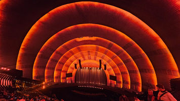 Warm orange arches inside an auditorium, viewed from the seating area toward the stage.
