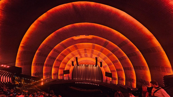 Warm orange arches inside an auditorium, viewed from the seating area toward the stage.